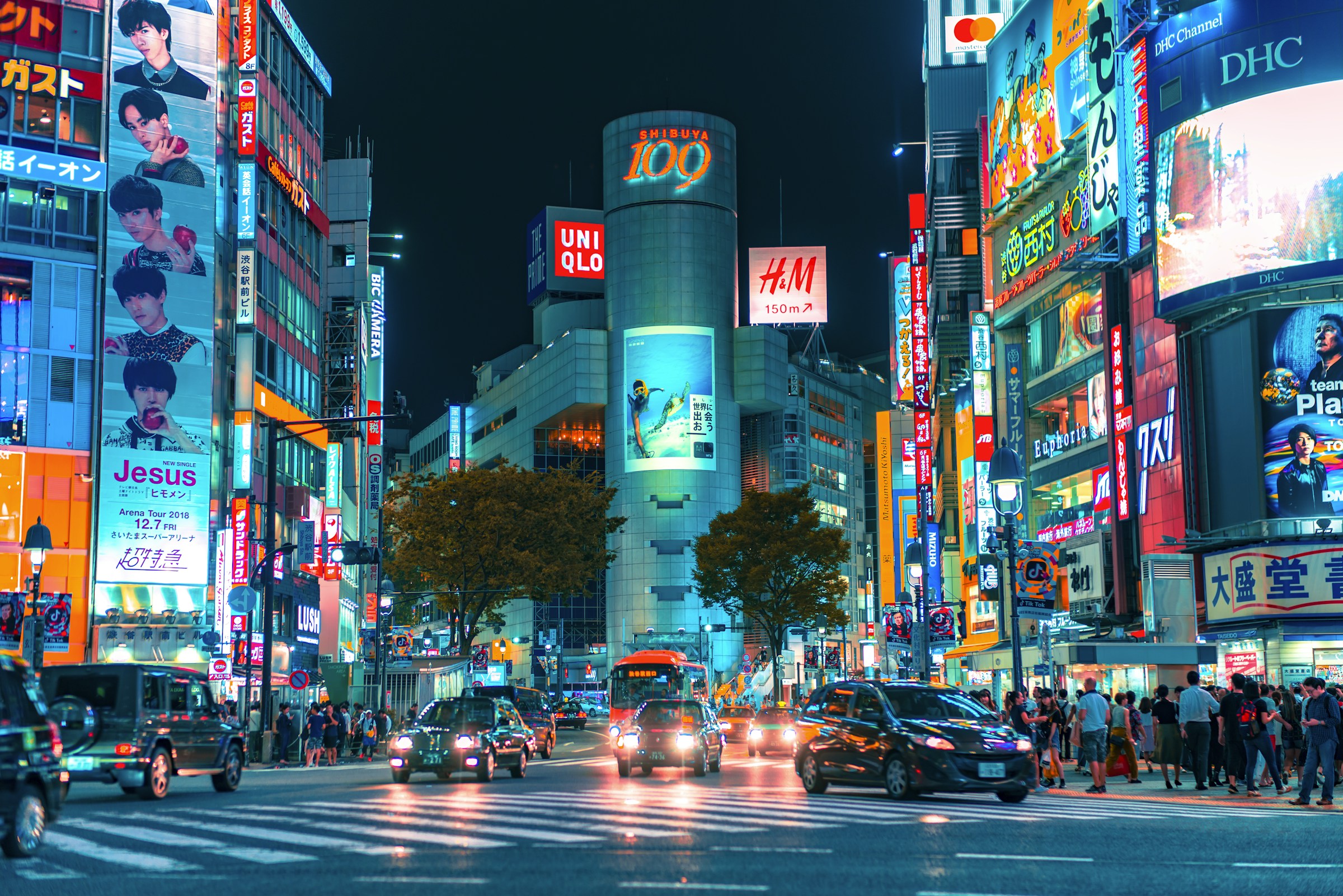 Cars driving through a neon-lit intersection in Shibuya, Tokyo, at night