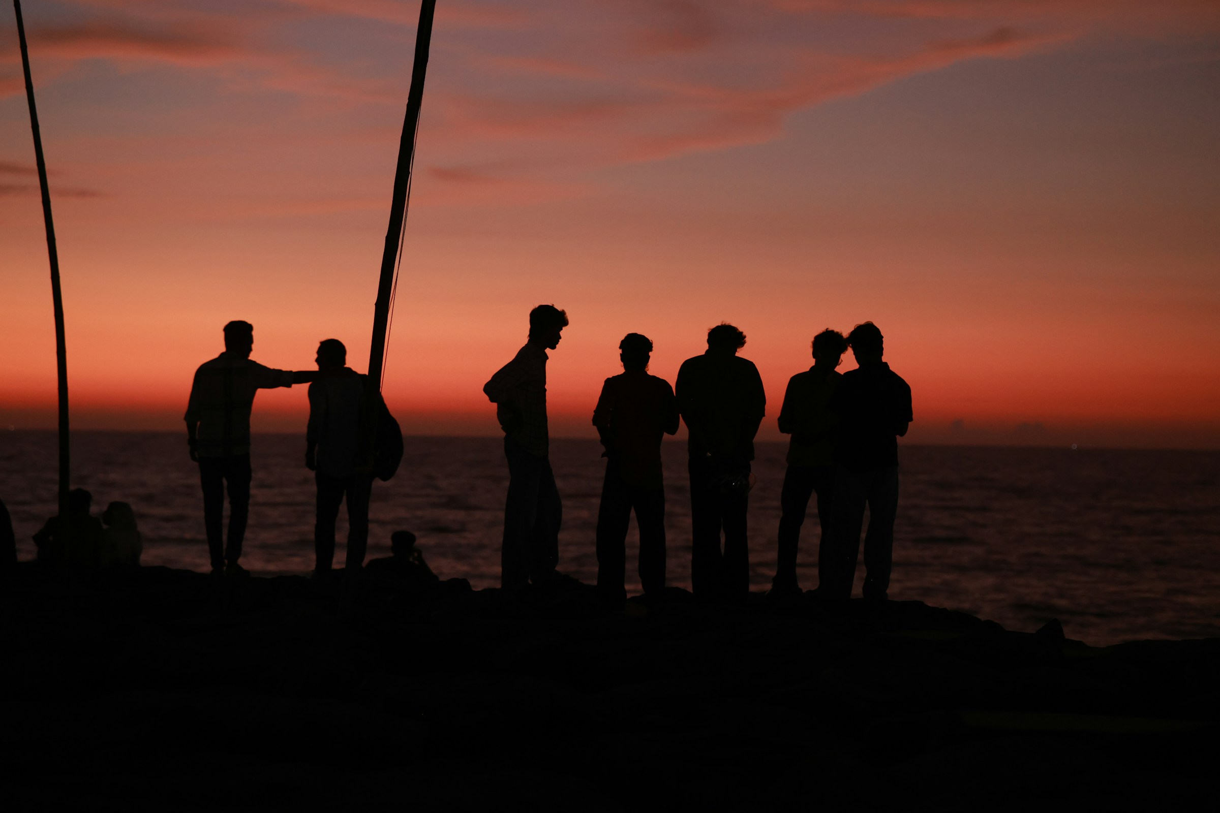 Silhouettes of a group of friends on a rocky shore against a warm orange sky